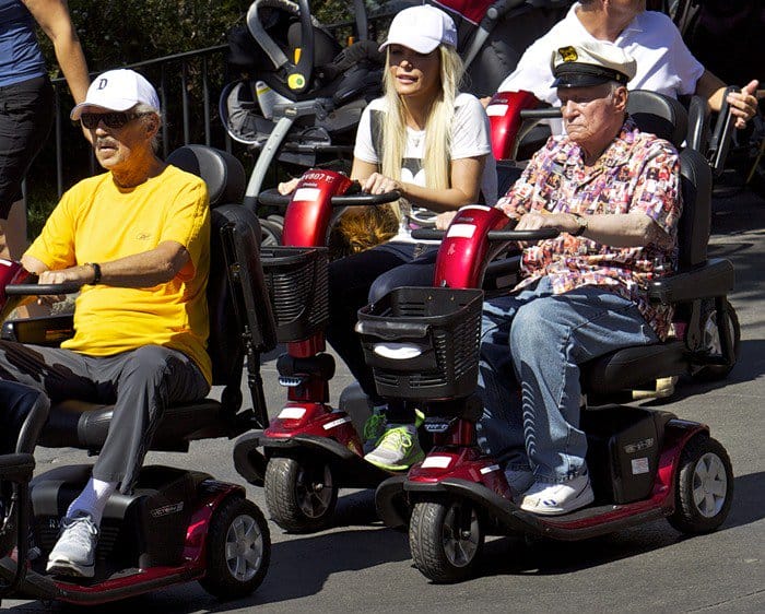 Hugh Hefner and Crystal Hefner ride mobility scooters through Disneyland Park