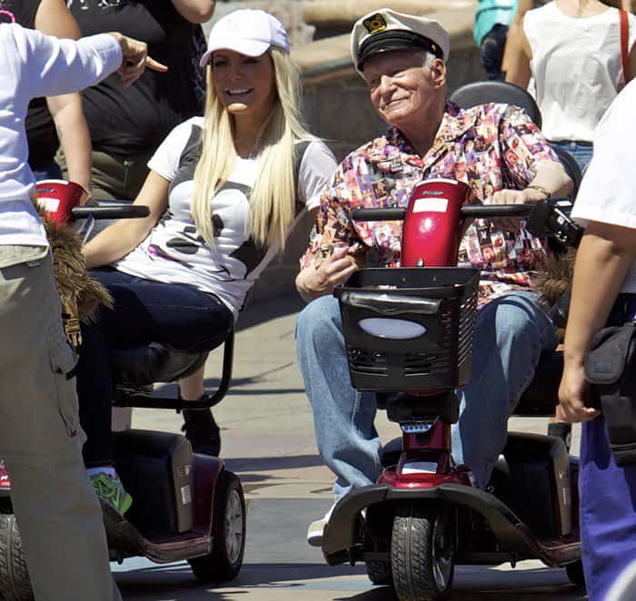 Hugh Hefner and Crystal Hefner ride mobility scooters through Disneyland Park