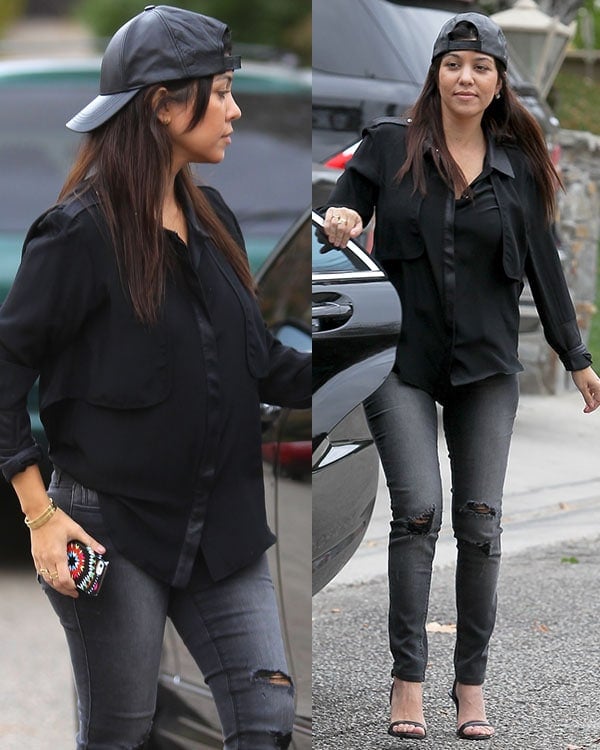 Kourtney Kardashian paired a loose collared, long-sleeved shirt in black with ripped dark-washed denims and styled with a baseball cap worn backward