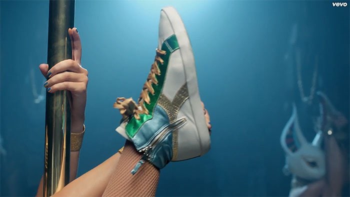 Katy does high kicks and splits in a pair of green-gold-and-blue high-top sneakers by Diadora