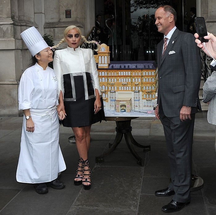 Lady Gaga posing with a very detailed custom cake in celebration of the 150th anniversary of London’s first grand hotel