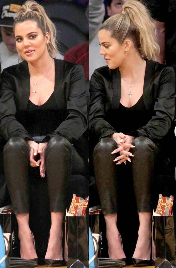 Khloe Kardashian wearing a black jacket, a black low-cut top, black leather leggings, and black pointy-toe pumps at the Lakers vs. Cavaliers basketball game