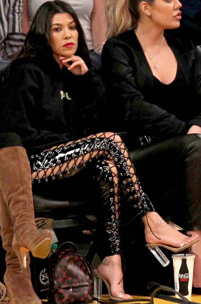 Kourtney Kardashian wearing a Yeezy sweatshirt, black lace-up leggings, and Yeezy sandals at the Lakers vs. Cavaliers basketball game