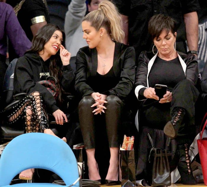 Kourtney Kardashian wearing Yeezy sandals, Khloe Kardashian wearing black pointy-toe pumps, and Kris Jenner wearing black lace-up booties at Lakers vs. Cavaliers basketball game