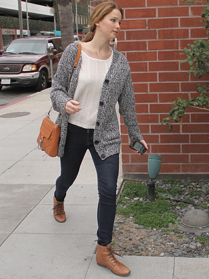 Jennifer Lawrence looked relaxed in fitted dark wash skinny jeans paired with a speckled grey oversized cardigan, a pleated cream top, and wearing light brown worker boots