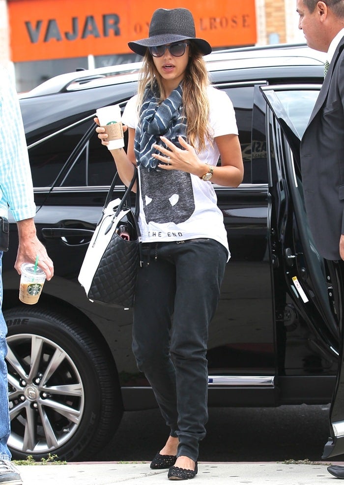 Jessica Alba wearing a printed white top by Zoe Karssen, faded black track pants by Ragdoll Los Angeles, basic flats, a floppy hat, and a scarf