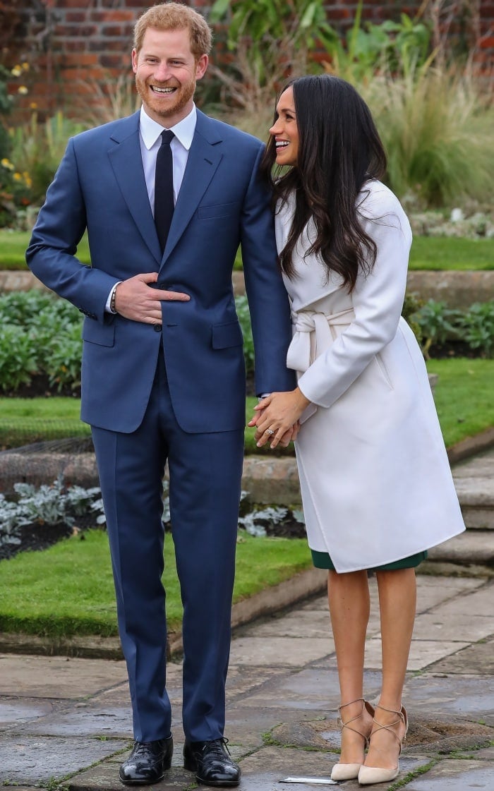 Prince Harry wearing a classic navy suit and Meghan Markle wearing a Line coat, P.A.R.O.S.H. dress, and Aquazzura heels