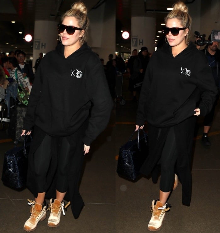 Khloe Kardashian wearing a black hoodie, cropped black leggings, and Timberland x Off-White leather lace-up boots at the Los Angeles International Airport