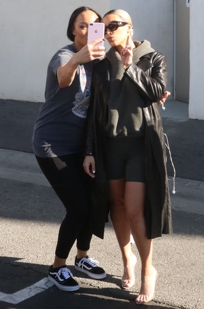 Kim Kardashian styled Kanye West's heels with a grey wool hoodie, knee-length skin tight biker shorts, a classic black leather overcoat, and Versace sunglasses