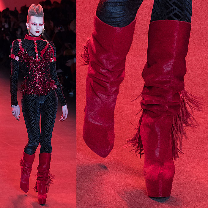 A model wearing red fringed slouchy boots with a red, leather-harnessed corset covered in glittery red talons.