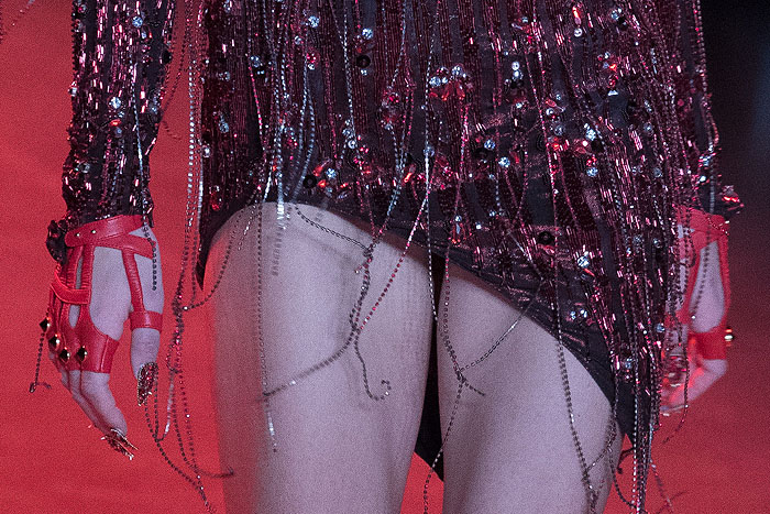 Model's chain-fringed, beaded, and sequined dress, red leather fingerless gloves, and gold-spiked, red-lacquered stiletto nails.