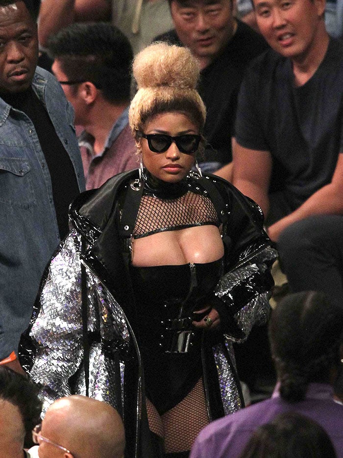 Nicki Minaj turning heads in a black latex zip bodysuit, fishnets, silver metal studs, and a scaly, silver hooded coat with black patent strips.