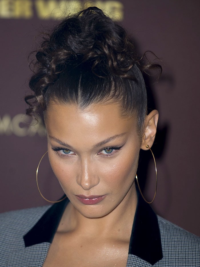 Bella Hadid with a curly top ponytail and gold hoop earrings.