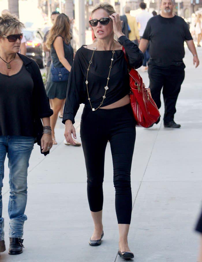 Sharon Stone elegantly contrasts her sleek all-black ensemble with a striking red patent purse, adding a vibrant touch to her look