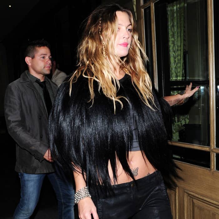 Drew Barrymore rocks a bold, edgy look with a midriff-baring Marni black goat fur cape, paired with distressed black cargo pants and silver accessories