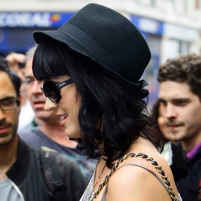 Katy Perry effortlessly elevates her look with a chic black fedora, adding a stylish edge to her signature dark waves and statement accessories