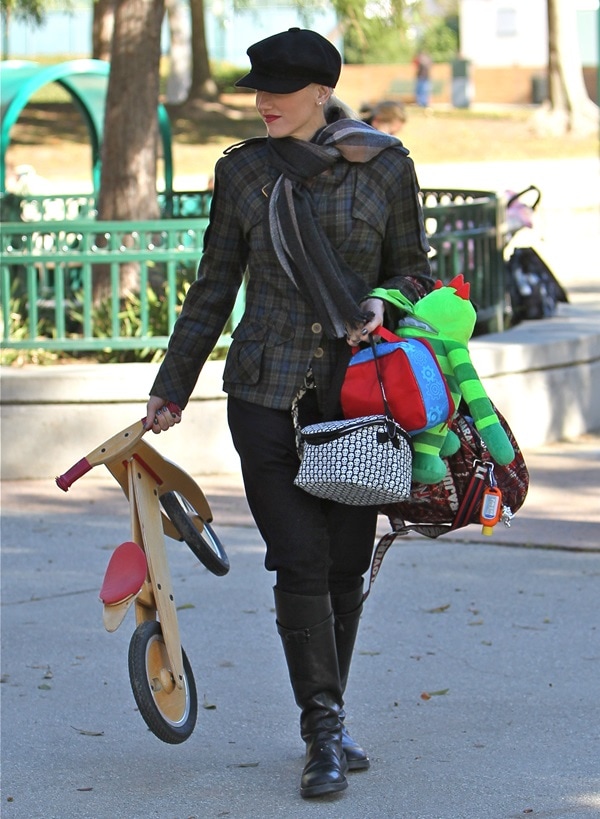 Gwen Stefani exudes chic equestrian-inspired style at a Los Angeles park on November 28, 2010, pairing a tailored L.A.M.B. British plaid jacket with sleek black riding boots, a newsboy cap, and a cozy scarf while juggling mom duties in effortless fashion