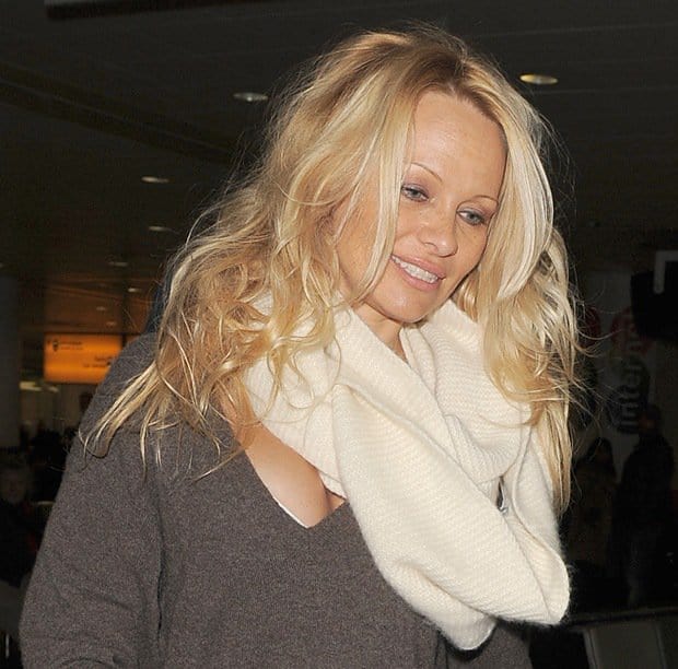 Pamela Anderson wearing a wintery, warm, creamy white scarf with a v-neck sweater dress which causes her large boobs to be visible