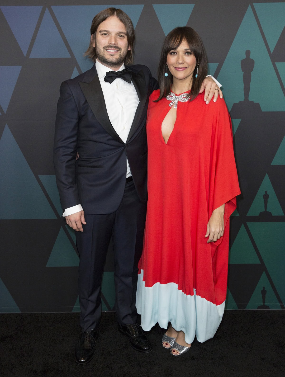 Rashida Jones dazzles in a red and pale blue Reem Acra kaftan dress paired with glittery Giuseppe Zanotti “Lavinia” heels at the 2018 Governors Awards with partner Ezra Koenig