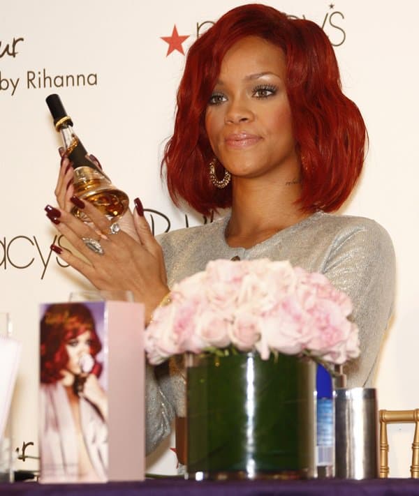 Rihanna elegantly showcases the Reb’l Fleur perfume bottle, featuring a sleek, tapered design with gold accents, as she debuts her signature fragrance at Macy’s