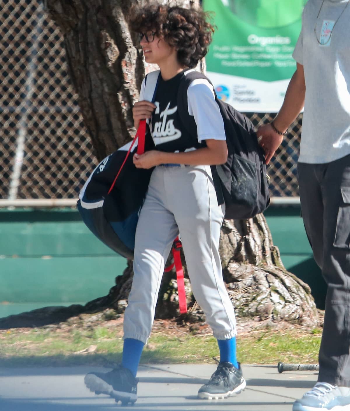 Emme Maribel Muñiz arrives at a baseball game in Los Angeles on April 29, 2022, dressed in sporty baseball gear, including cropped gray pants, a black-and-white team shirt, and cleats