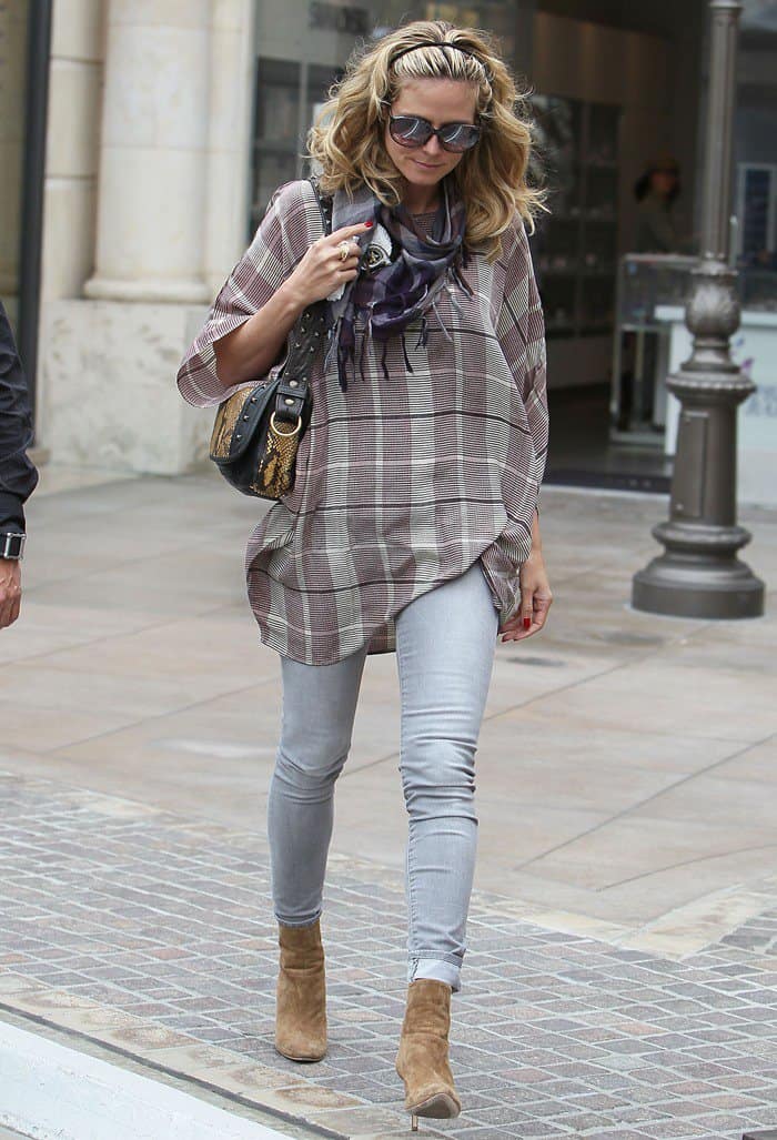 Heidi Klum elevates her casual-chic look with suede high-heeled ankle boots, pairing them effortlessly with skinny jeans, a plaid tunic, and a skull-embroidered scarf
