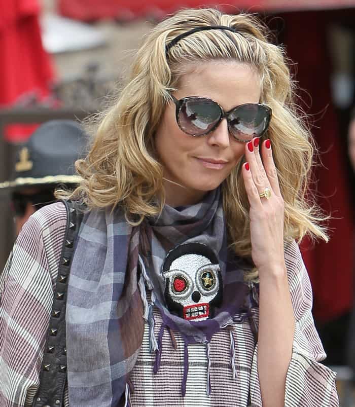 Heidi Klum adds an edgy twist to her casual plaid ensemble with a skull-embroidered scarf, oversized sunglasses, and a studded leather bag