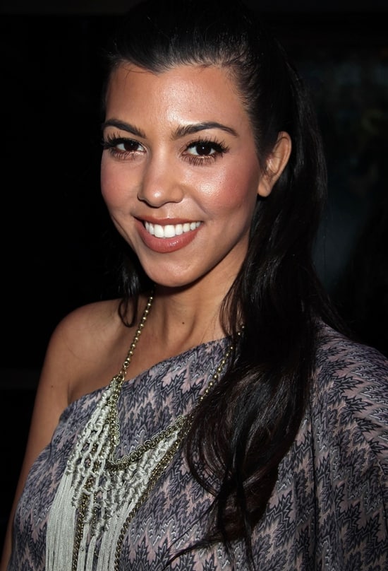 Kourtney Kardashian exudes boho-chic elegance in a patterned one-shoulder maxi dress, accessorized with layered fringe necklaces and soft waves, adding a touch of effortless glamour