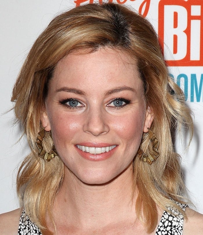 Elizabeth Banks stuns with soft waves and natural makeup, complemented by statement gold earrings, perfectly framing her glowing complexion at the Hollywood Bites Back event