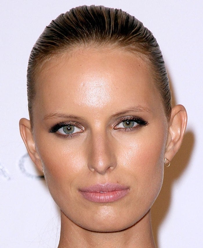 Karolina Kurkova enhances her striking green eyes with soft smoky makeup, complementing her sleek, pulled-back hairstyle and delicate gold hoop earrings
