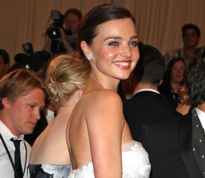 Miranda Kerr radiates elegance with a sleek, low chignon hairstyle, dewy skin, rosy cheeks, and a glossy pink lip