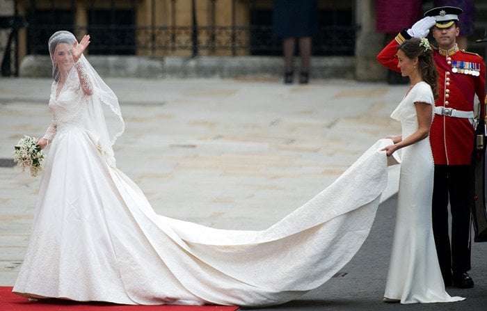 Kate Middleton waves to the crowds as her sister and maid of honor, Pippa Middleton, holds the train of her wedding dress