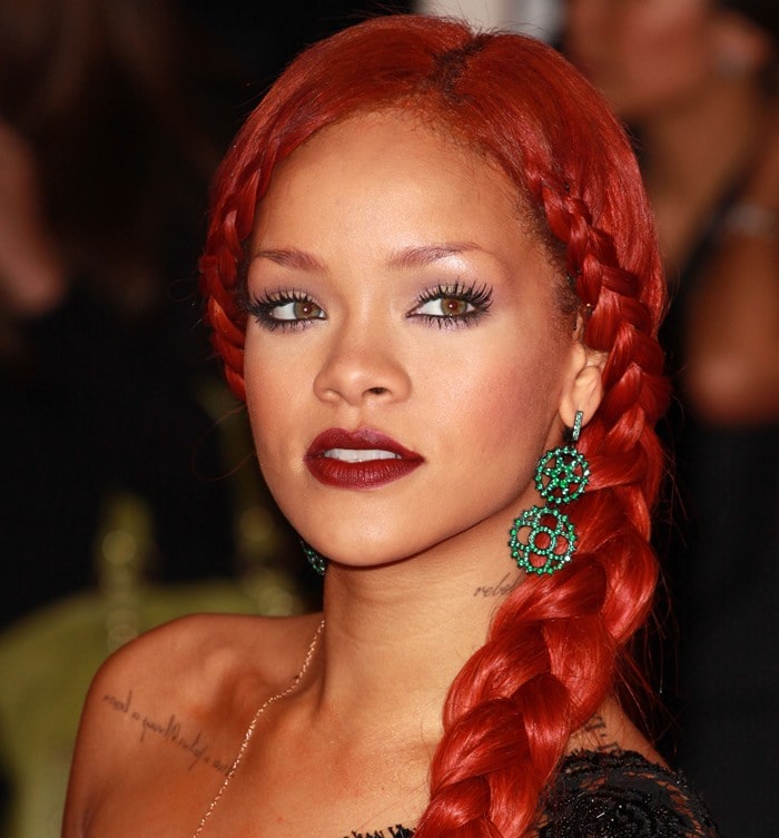 Rihanna's fiery red hair, styled in sleek double braids, perfectly complemented her striking green dangling earrings, creating a bold and elegant contrast