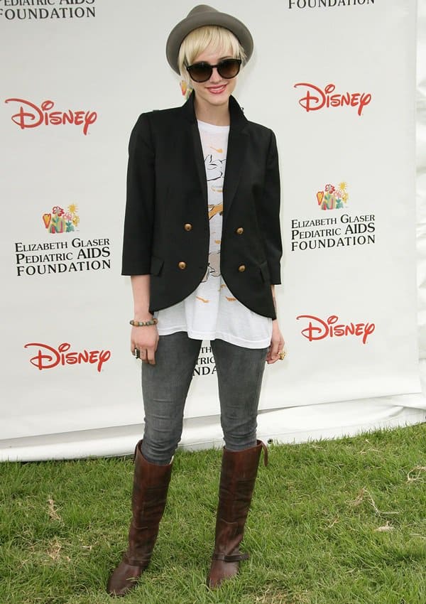 Ashlee Simpson stuns in a tailored black blazer, slate James Jeans Twiggy leggings, a casual graphic tee, knee-high brown boots, and a chic bowler hat
