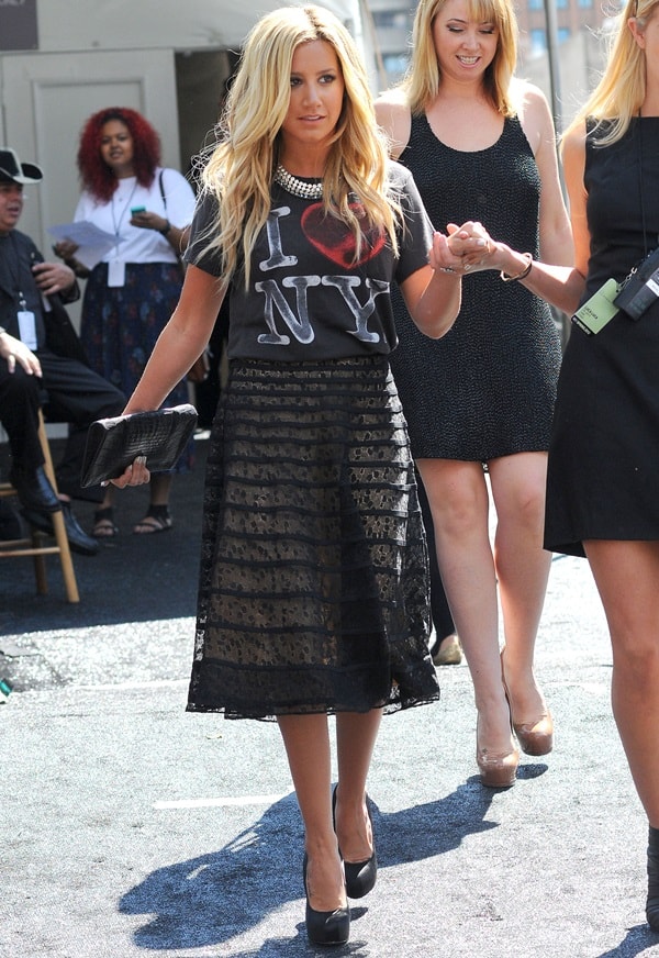 On September 8, 2011, Ashley Tisdale was seen in NYC wearing a Junk Food I Love NY T-shirt, a Luca Luca Fall 2011 RTW overlay knee-length skirt, Brian Atwood Maniac pumps in black satin, and a Kelly Locke Bleeker clutch