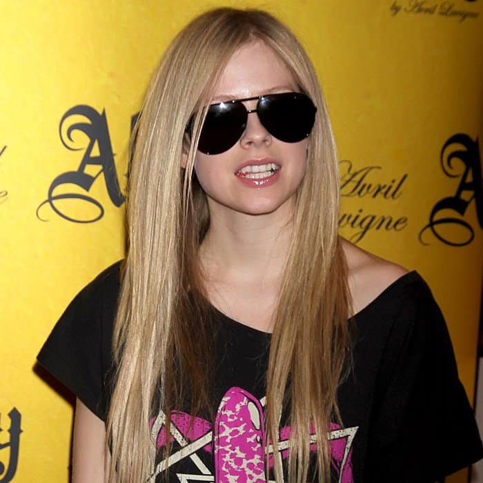 Avril Lavigne rocks her signature sleek, straight blonde hair with oversized black aviator sunglasses, adding a cool, effortless edge to her punk-inspired look