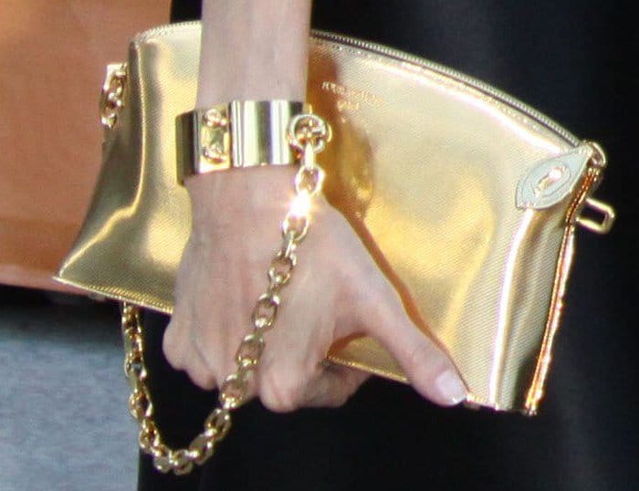 Angelina Jolie totes a gold Louis Vuitton Lockit PM Devotion clutch with a cuff wrapped around her wrist