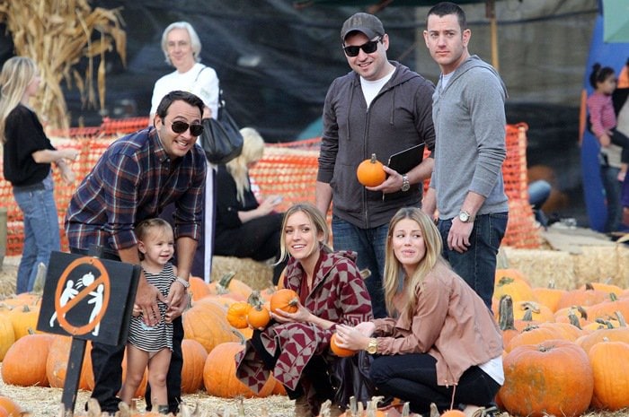 Embracing autumn's charm, Kristin Cavallari elegantly dons a cozy, geometric-patterned blanket cardigan in shades of gray and maroon during her festive pumpkin-picking adventure