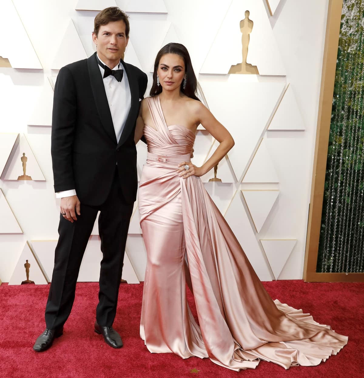 Ashton Kutcher in a black tuxedo and Mila Kunis in a light pink belted Zuhair Murad Spring 2022 Couture dress attend the 94th Annual Academy Awards