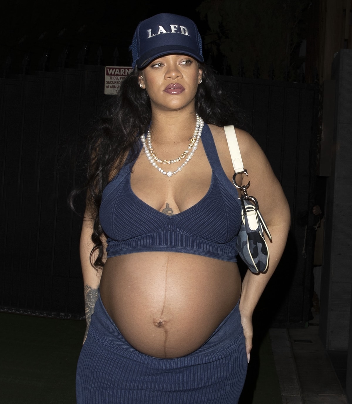 Rihanna shows off her huge baby bump in a denim crop top paired with a rib-knit maxi skirt from Alaïa and an LAFD hat