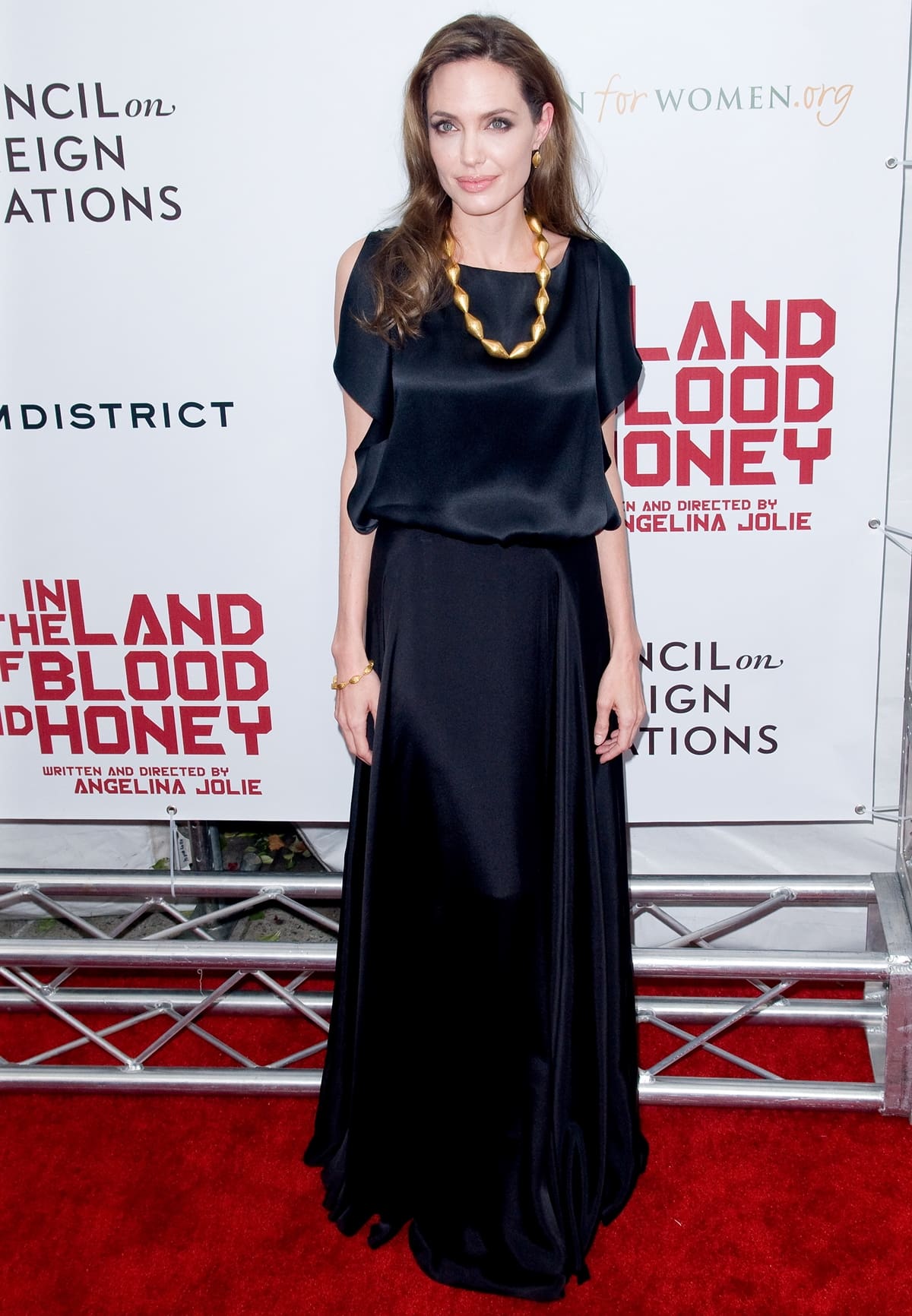 Angelina Jolie wears a black satin cold-shoulder blouse with a black Ralph Lauren maxi skirt and a gold Ofira necklace