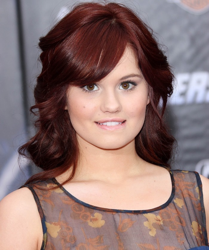 Debby Ryan stuns with her voluminous auburn curls, subtle makeup, and a sheer floral dress that perfectly complements her fresh and natural look