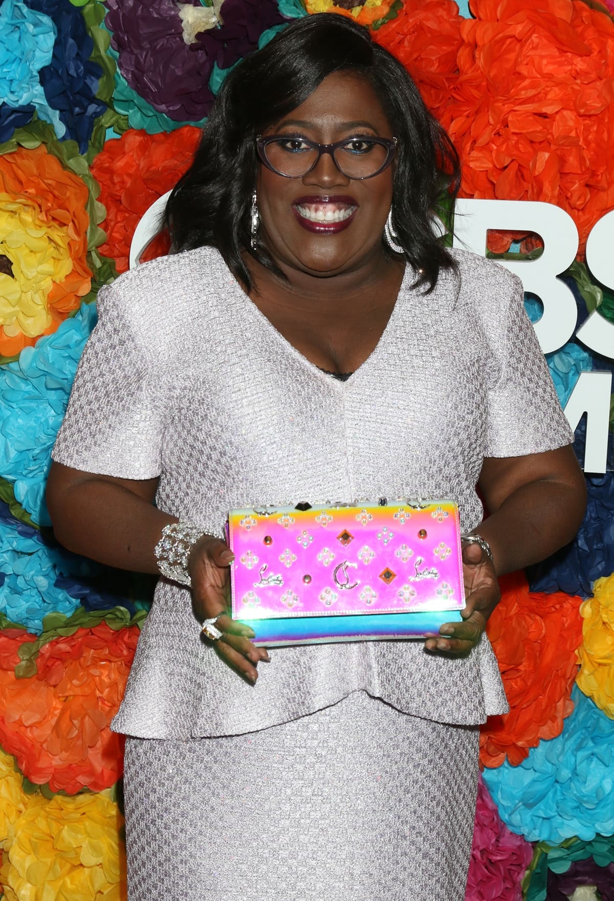 Sheryl Underwood shines in a sparkling lavender ensemble, holding a vibrant pink and gold embellished clutch at a star-studded event