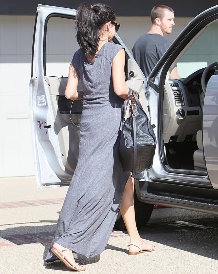 Selena Gomez wears a trendy grey maxi dress with Zara laminated chain sandals, showcasing the flat gold-accented footwear as she steps into a car with her Louis Vuitton Lumineuse GM shoulder bag at Joel Silver's Memorial Day party in Malibu on May 28, 2012