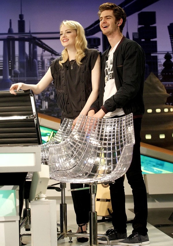 Emma Stone wears a gray silk blouse with casual pants during a TV appearance with Andrew Garfield