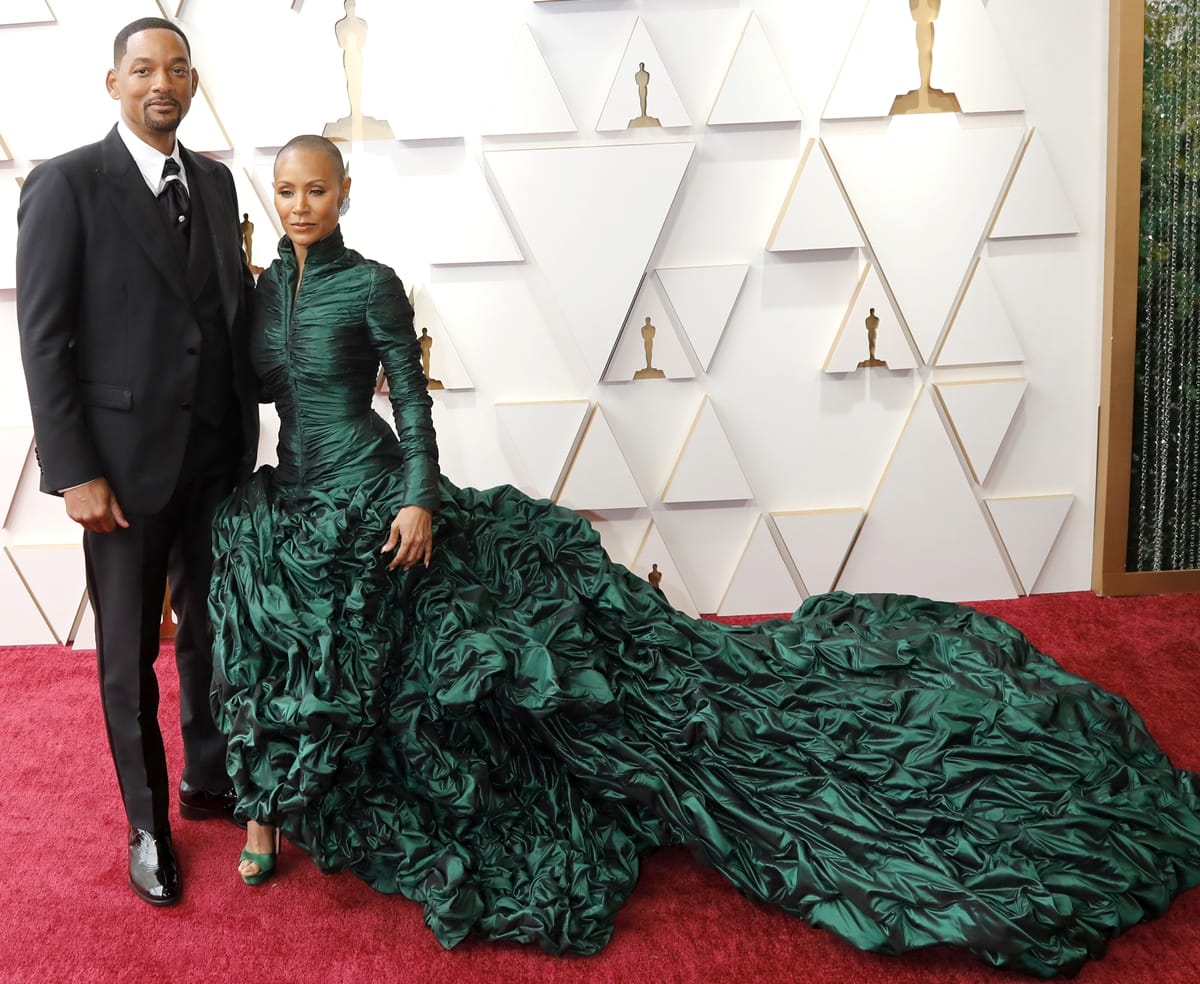 Will Smith in a black Dolce and Gabbana 3-piece suit and his wife Jada Pinkett Smith in a dark green Jean Paul Gaultier ruffled gown on the red carpet at the 2022 Academy Awards