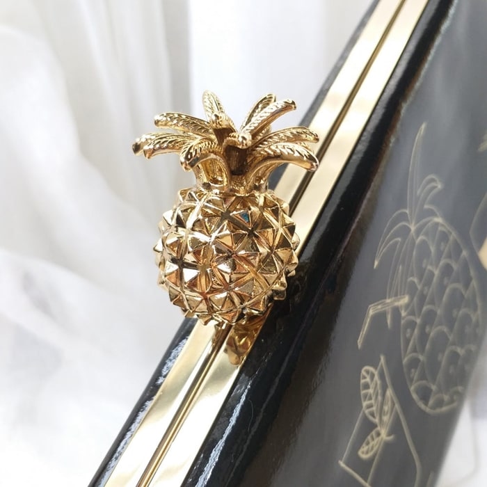 The exquisite detail of Kate Spade's clutch is crowned with a unique gold pineapple-shaped clasp, adding a touch of tropical glamour to the piece