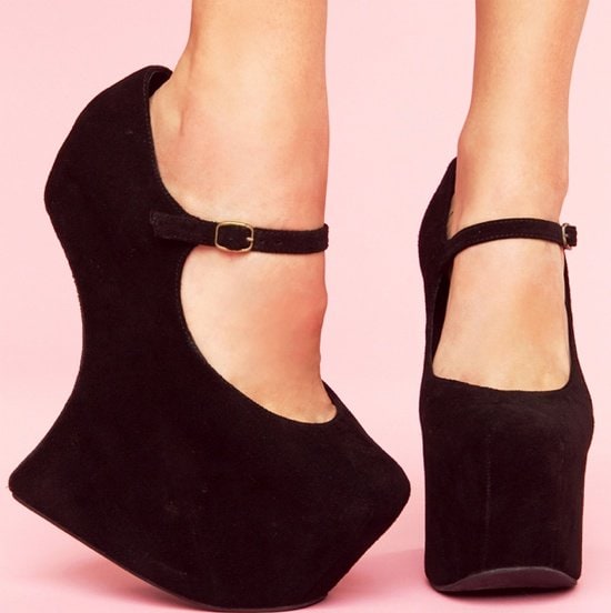 A dainty mary-jane strap details a dark suede pump set upon a stunning sculpted wedge heel