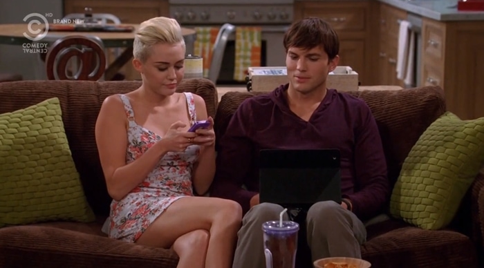 Miley Cyrus, as Missi, channels casual charm in a flirty floral sundress while sharing a scene with Ashton Kutcher on Two and a Half Men