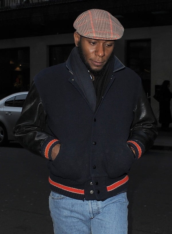 American rapper and actor Mos Def wears a varsity jacket with a brown newsboy cap